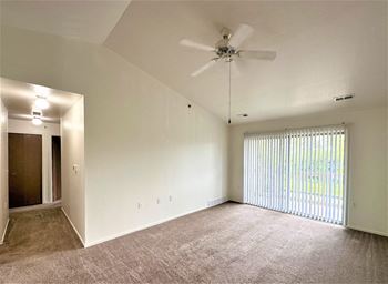 An empty living room with a ceiling fan and a window